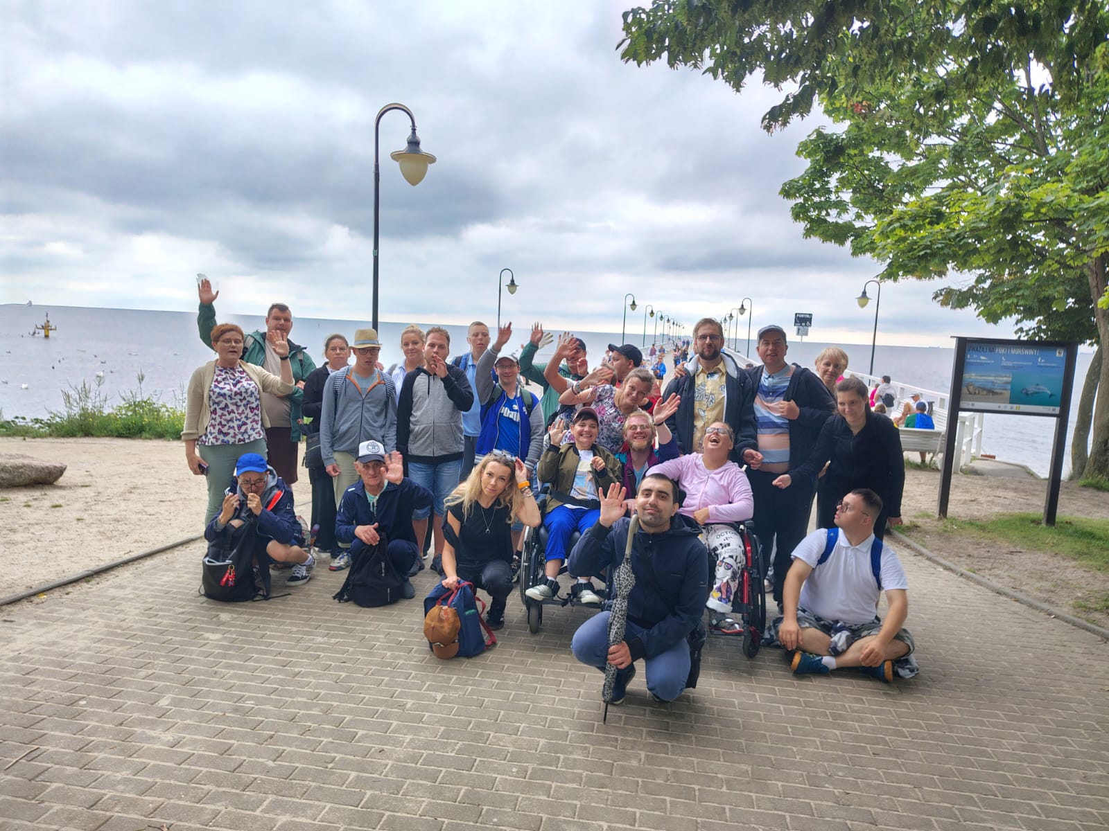 Grupa 16 uczestników i 7 terapeutów ŚDS Wejherowo na tle molo w Orłowie, plaży i morza