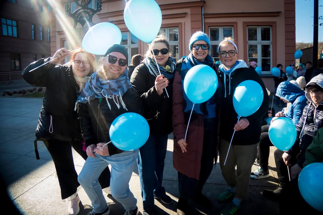 Grupa osób pozuje do zdjęcia z niebieskimi balonami przed budynkiem.